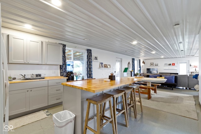 kitchen with wood counters, a kitchen breakfast bar, gray cabinetry, and sink