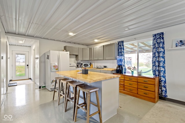 kitchen featuring butcher block countertops, plenty of natural light, white appliances, and a breakfast bar area