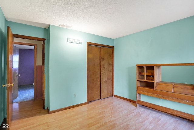 unfurnished bedroom with a textured ceiling, a closet, and light hardwood / wood-style flooring