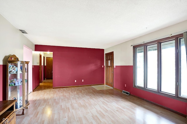 empty room with a textured ceiling and light hardwood / wood-style flooring