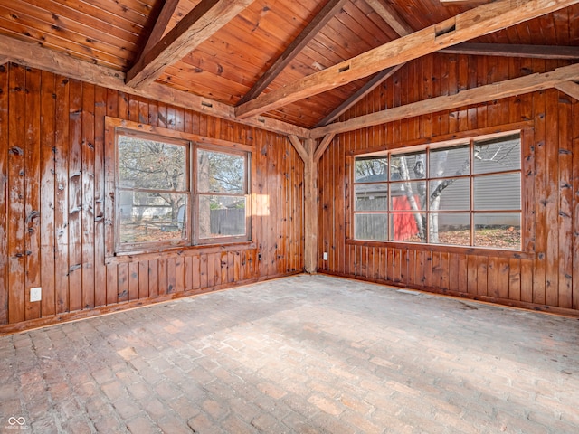 empty room with wood walls, a wealth of natural light, wood ceiling, and vaulted ceiling with beams