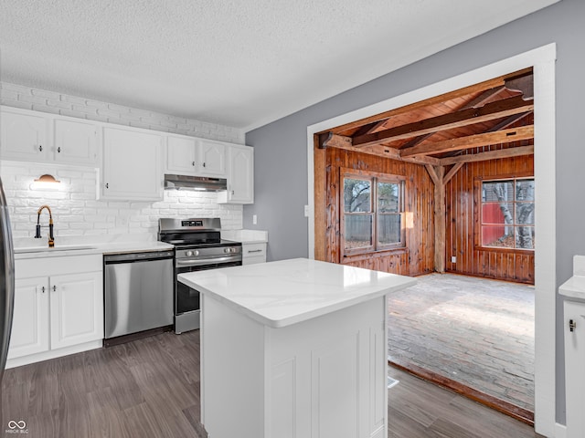 kitchen featuring white cabinetry, sink, appliances with stainless steel finishes, dark wood-type flooring, and wooden walls