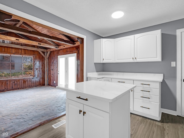 kitchen featuring vaulted ceiling with beams, a kitchen island, wooden walls, light hardwood / wood-style floors, and white cabinets