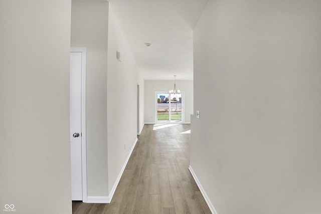 hallway featuring wood-type flooring and an inviting chandelier