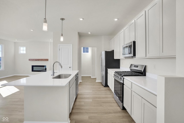 kitchen featuring stainless steel appliances, light hardwood / wood-style floors, sink, decorative light fixtures, and an island with sink