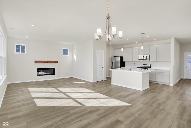 kitchen featuring pendant lighting, light wood-type flooring, appliances with stainless steel finishes, and a center island with sink