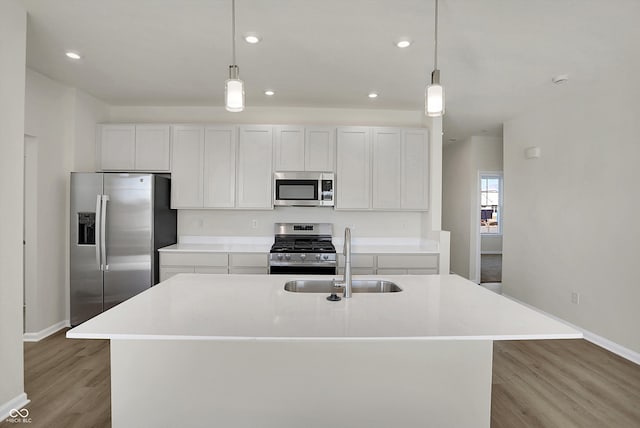 kitchen featuring light wood-type flooring, appliances with stainless steel finishes, hanging light fixtures, sink, and a kitchen island with sink