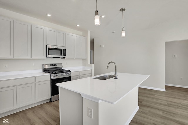 kitchen with a center island with sink, sink, appliances with stainless steel finishes, decorative light fixtures, and light hardwood / wood-style flooring