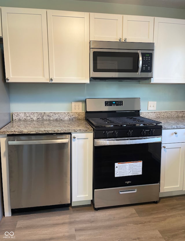 kitchen with appliances with stainless steel finishes, light stone counters, light hardwood / wood-style floors, and white cabinets