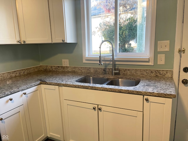 kitchen with white cabinetry, sink, and light stone countertops