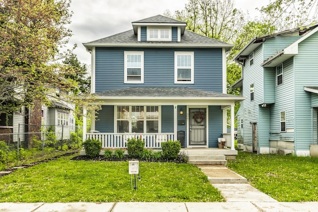 american foursquare style home featuring a porch, fence, a shingled roof, and a front lawn