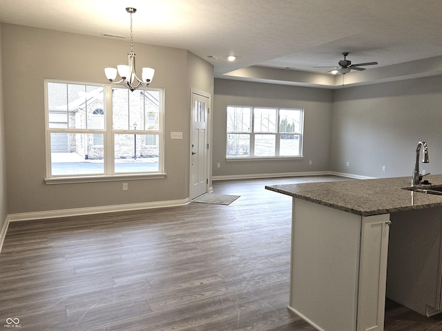 kitchen featuring a raised ceiling, decorative light fixtures, sink, dark wood-type flooring, and dark stone countertops