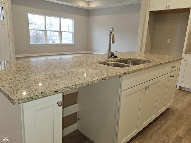 kitchen with light stone counters, sink, white cabinetry, and an island with sink