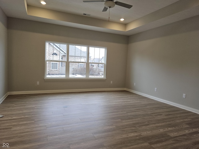 unfurnished room with ceiling fan, dark wood-type flooring, and a raised ceiling