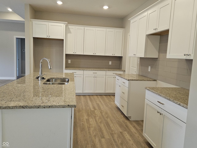 kitchen featuring sink, white cabinets, light hardwood / wood-style floors, and an island with sink