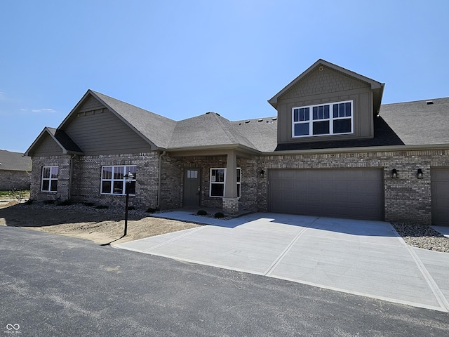 craftsman-style home featuring concrete driveway, brick siding, a shingled roof, and a garage