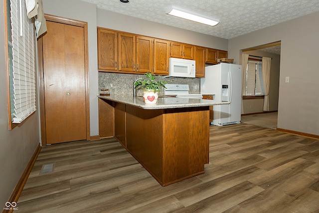 kitchen with a textured ceiling, kitchen peninsula, dark wood-type flooring, and white appliances