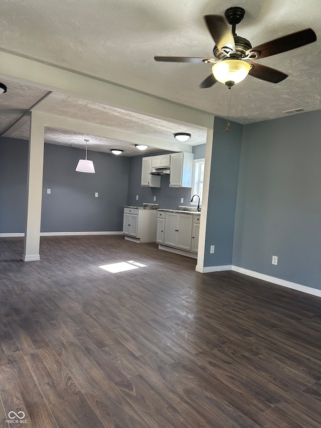 unfurnished living room featuring ceiling fan, dark hardwood / wood-style floors, a textured ceiling, and sink