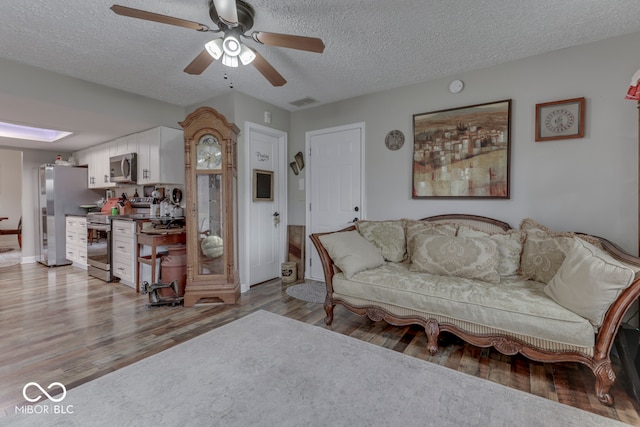 living room with light hardwood / wood-style floors, a textured ceiling, and ceiling fan