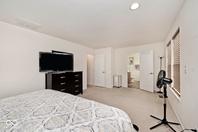 bedroom featuring a textured ceiling, light colored carpet, and ensuite bathroom