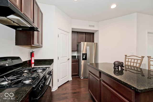 kitchen featuring dark hardwood / wood-style flooring, gas stove, range hood, dark stone countertops, and stainless steel fridge