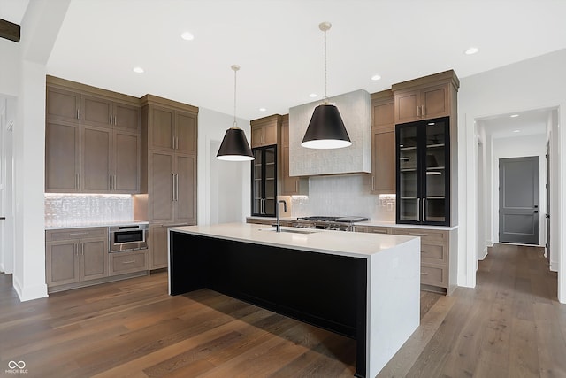 kitchen with a large island with sink, hanging light fixtures, dark hardwood / wood-style floors, and backsplash