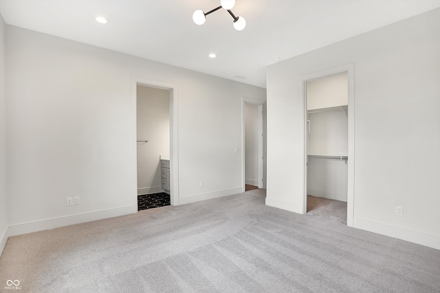 unfurnished bedroom featuring ensuite bath, a spacious closet, light colored carpet, and a closet