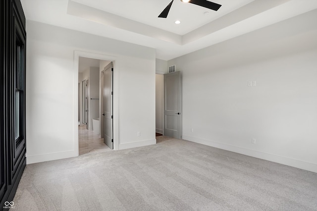 unfurnished bedroom featuring light colored carpet, ceiling fan, and a tray ceiling