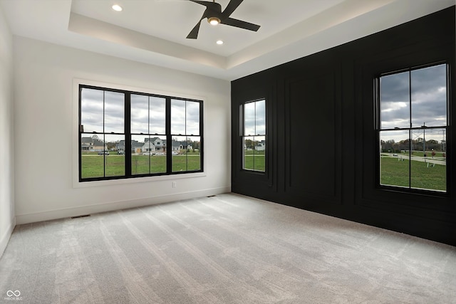 carpeted empty room with a healthy amount of sunlight, ceiling fan, and a tray ceiling