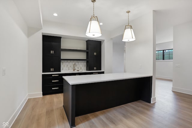 kitchen featuring backsplash, hanging light fixtures, sink, and light hardwood / wood-style floors