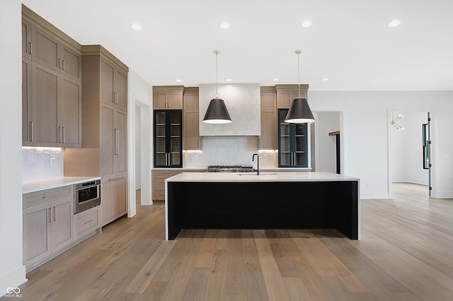 kitchen featuring light hardwood / wood-style floors, sink, tasteful backsplash, decorative light fixtures, and a spacious island