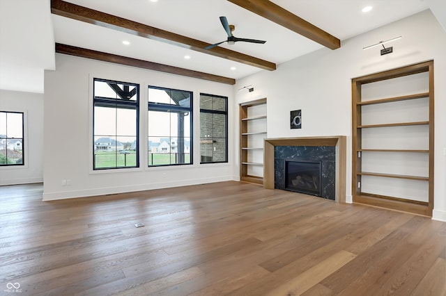 unfurnished living room featuring beamed ceiling, built in shelves, ceiling fan, hardwood / wood-style floors, and a fireplace