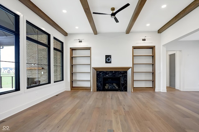 unfurnished living room featuring a fireplace, light wood-type flooring, ceiling fan, and beamed ceiling