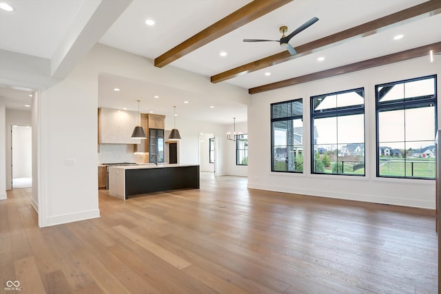 unfurnished living room featuring sink, beamed ceiling, hardwood / wood-style floors, and ceiling fan with notable chandelier