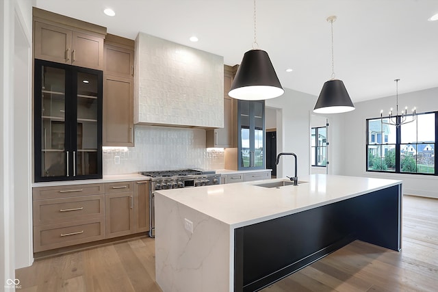 kitchen featuring a center island with sink, sink, stainless steel range, pendant lighting, and light hardwood / wood-style flooring