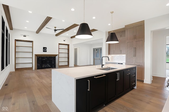 kitchen featuring a kitchen island with sink, beam ceiling, sink, and pendant lighting