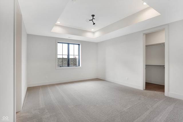 unfurnished bedroom featuring a walk in closet, light colored carpet, a tray ceiling, and a closet