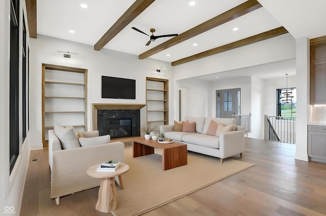 living room featuring beamed ceiling, a high end fireplace, ceiling fan, and light hardwood / wood-style flooring