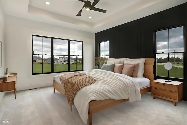 bedroom featuring ceiling fan, a raised ceiling, and light colored carpet