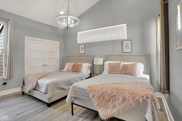 bedroom with wood-type flooring, a closet, lofted ceiling, and a notable chandelier