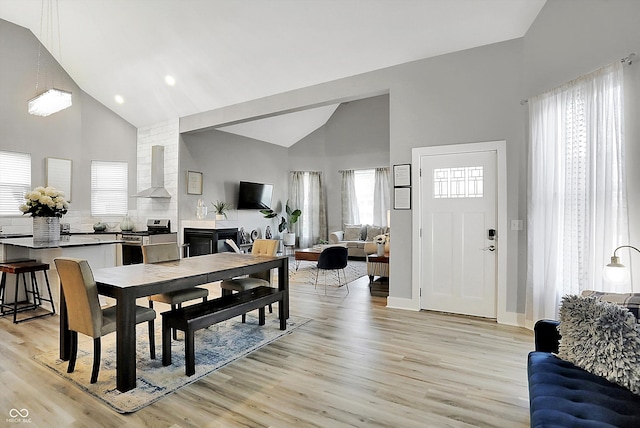 dining space with high vaulted ceiling, light hardwood / wood-style flooring, and a healthy amount of sunlight