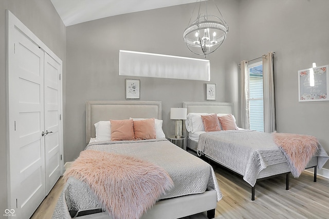 bedroom with light hardwood / wood-style floors, an inviting chandelier, a closet, and lofted ceiling