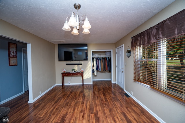 unfurnished dining area featuring an inviting chandelier, dark hardwood / wood-style floors, and a textured ceiling