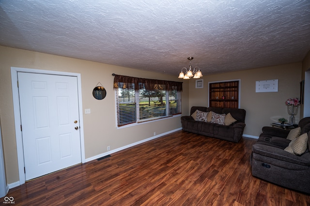 living room featuring dark wood-type flooring, a textured ceiling, and an inviting chandelier