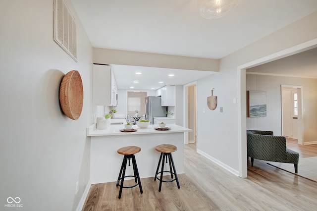 kitchen with a kitchen bar, kitchen peninsula, stainless steel refrigerator, white cabinetry, and light hardwood / wood-style flooring