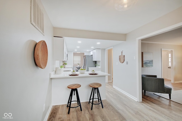 4902 N Capitol Ave, Indianapolis, IN 46208 - kitchen with freestanding refrigerator, a kitchen breakfast bar, light wood-style floors, white cabinetry, and light countertops