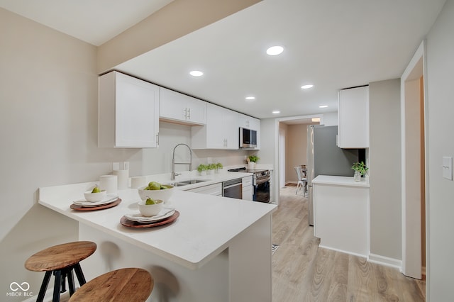 kitchen featuring stainless steel appliances, sink, a breakfast bar area, white cabinetry, and light wood-type flooring