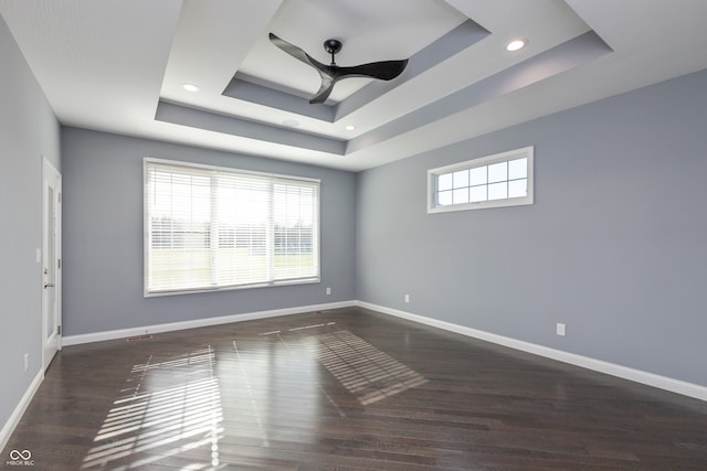 empty room featuring a tray ceiling, dark wood-type flooring, and a healthy amount of sunlight