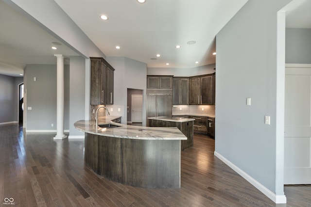 kitchen with dark hardwood / wood-style floors, light stone counters, sink, and decorative columns