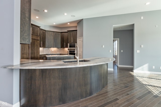 kitchen with dark wood-type flooring, backsplash, kitchen peninsula, dark brown cabinets, and appliances with stainless steel finishes